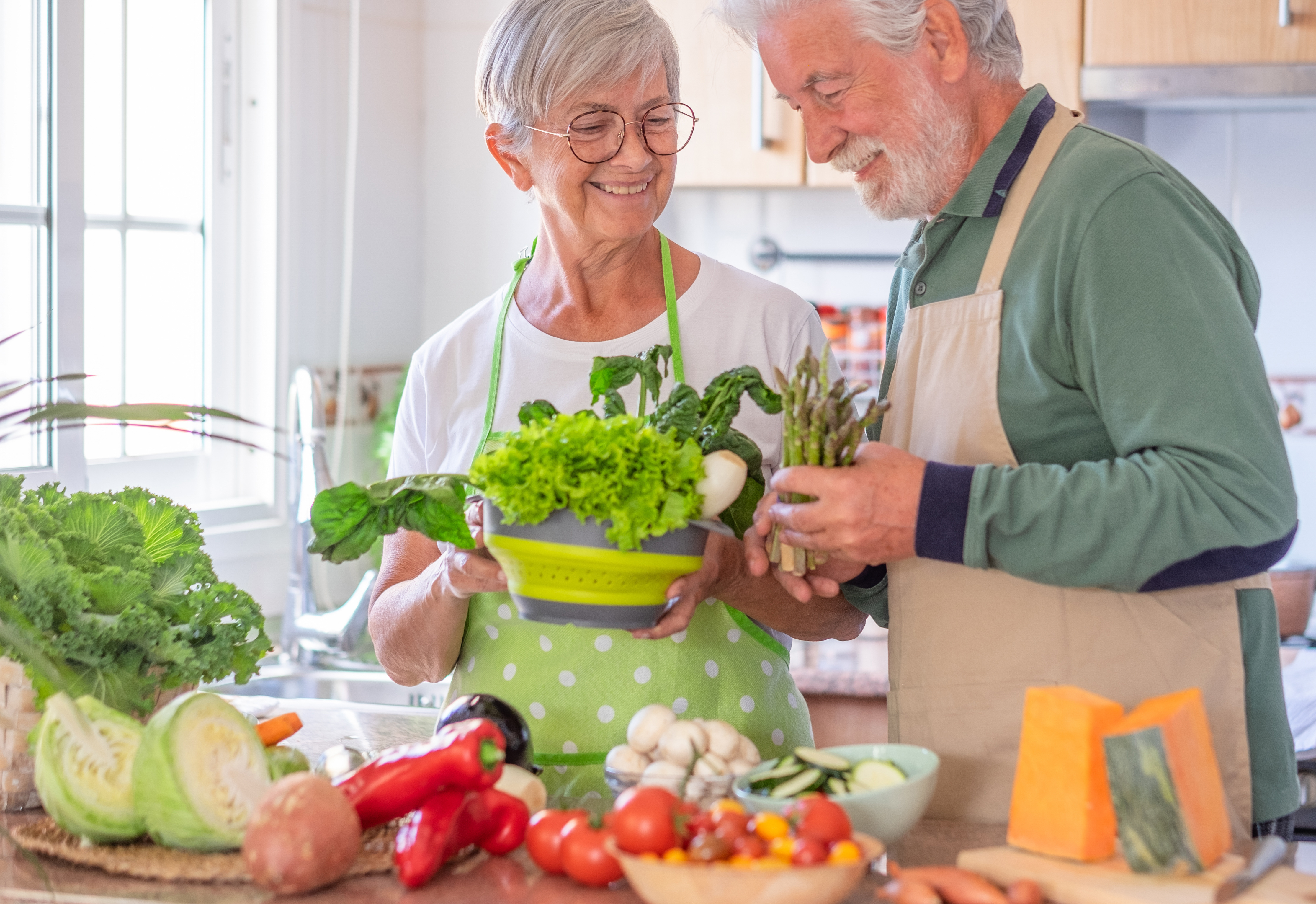 Attractive senior couple preparing vegetables together in the home kitchen. Caucasian elderly people enjoying healthy eating