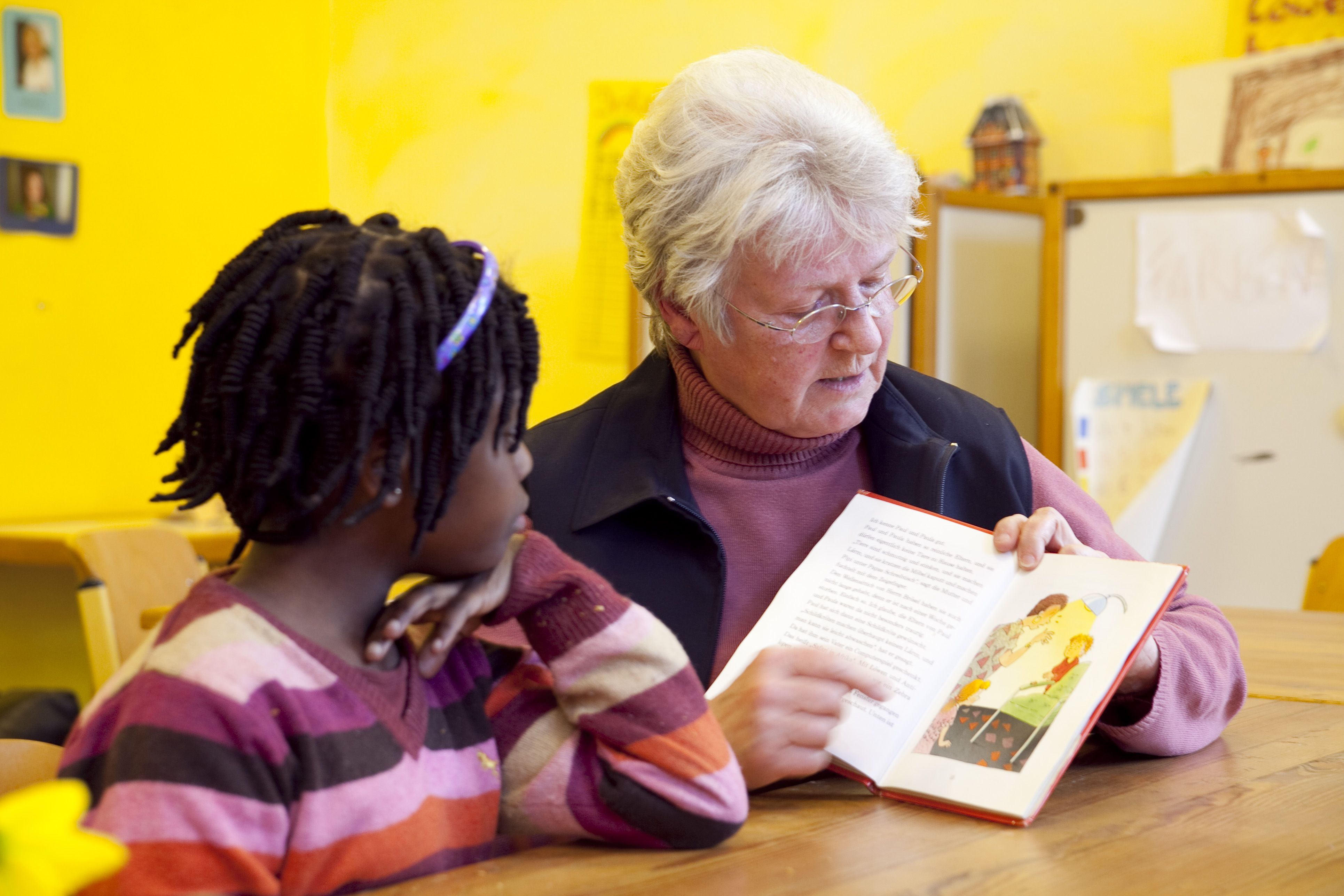 Eine ältere Freiwillige liest mit einem Kind ein Buch